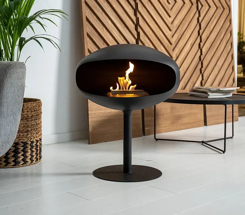 Cocoon Fires Pedestal bioethanol fireplace freestanding on the floor in front of a wooden panel wall